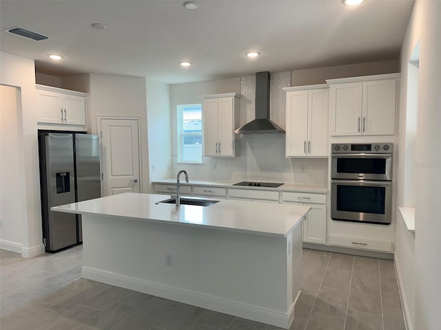 kitchen featuring wall chimney exhaust hood, sink, white cabinetry, stainless steel appliances, and a kitchen island with sink