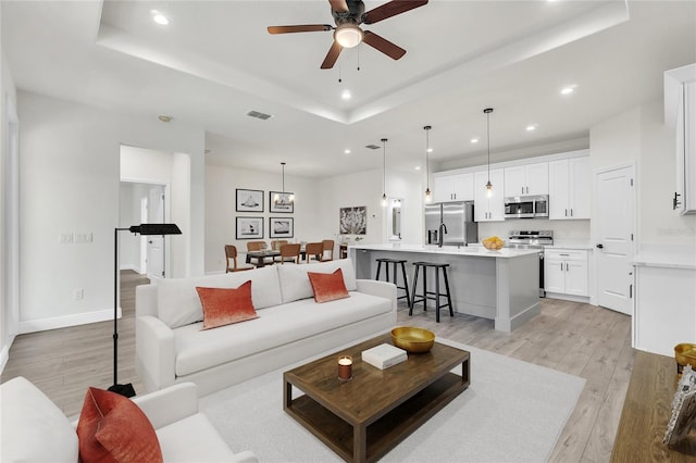 living room featuring a tray ceiling, ceiling fan, and light wood-type flooring