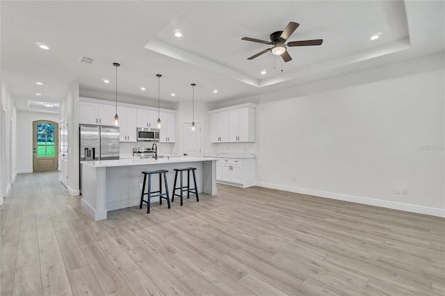 kitchen with appliances with stainless steel finishes, a tray ceiling, white cabinetry, and a spacious island