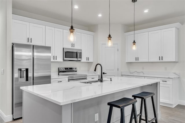 kitchen with white cabinets, sink, appliances with stainless steel finishes, and an island with sink