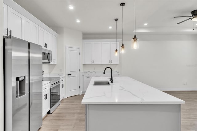 kitchen featuring appliances with stainless steel finishes, decorative light fixtures, white cabinetry, and a kitchen island with sink