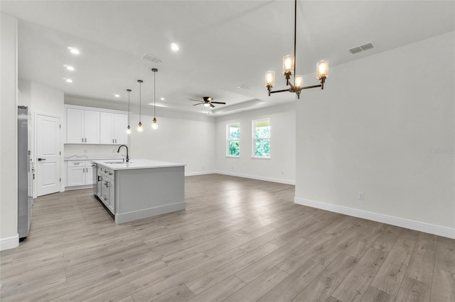 kitchen with pendant lighting, ceiling fan with notable chandelier, light hardwood / wood-style floors, and an island with sink