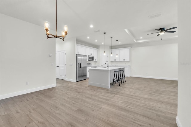 kitchen featuring light hardwood / wood-style flooring, pendant lighting, a kitchen island with sink, ceiling fan with notable chandelier, and appliances with stainless steel finishes