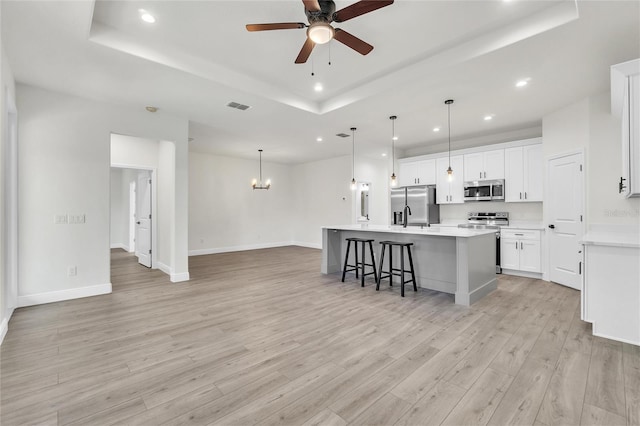 kitchen featuring a center island with sink, white cabinets, light wood-type flooring, appliances with stainless steel finishes, and a tray ceiling