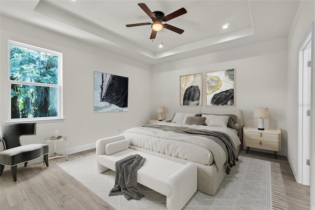 bedroom with ceiling fan, a raised ceiling, and light wood-type flooring