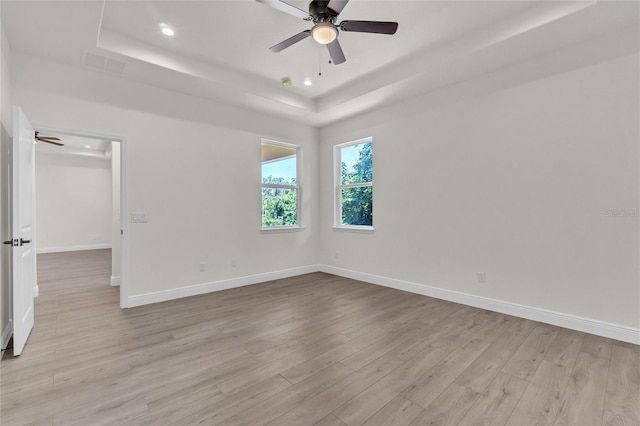 unfurnished room featuring ceiling fan, a raised ceiling, and light wood-type flooring