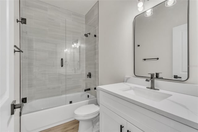 full bathroom featuring hardwood / wood-style floors, vanity, combined bath / shower with glass door, and toilet