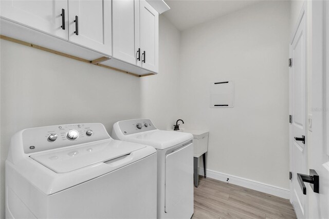 clothes washing area featuring cabinets, washing machine and dryer, and light hardwood / wood-style flooring