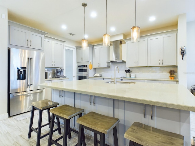 kitchen with sink, stainless steel appliances, wall chimney range hood, pendant lighting, and a kitchen bar