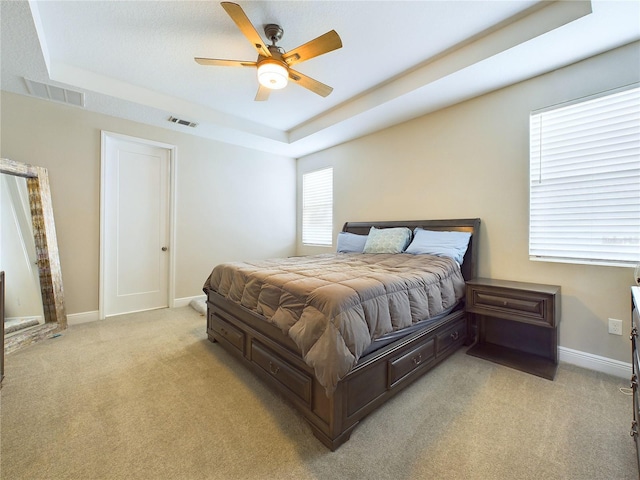 bedroom featuring light carpet, a tray ceiling, and ceiling fan