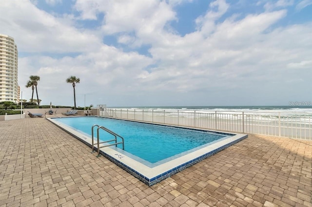 view of swimming pool featuring a patio area, a water view, and a view of the beach