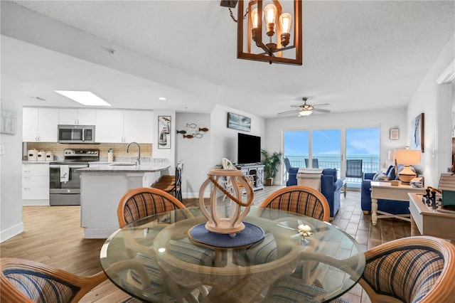 dining area featuring a skylight, ceiling fan, sink, light hardwood / wood-style floors, and a textured ceiling