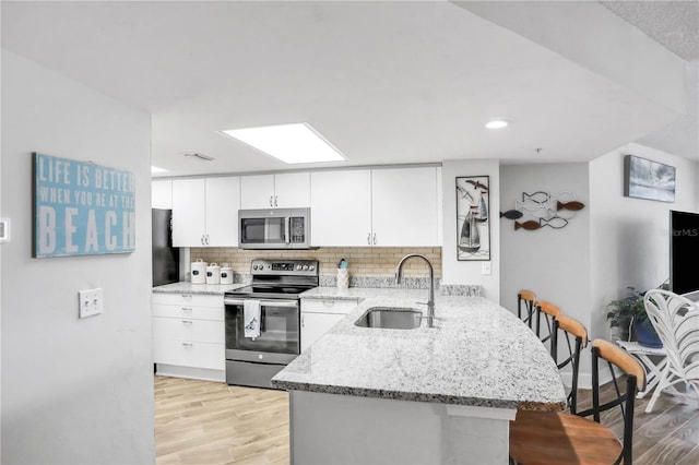 kitchen featuring kitchen peninsula, appliances with stainless steel finishes, light wood-type flooring, sink, and white cabinetry