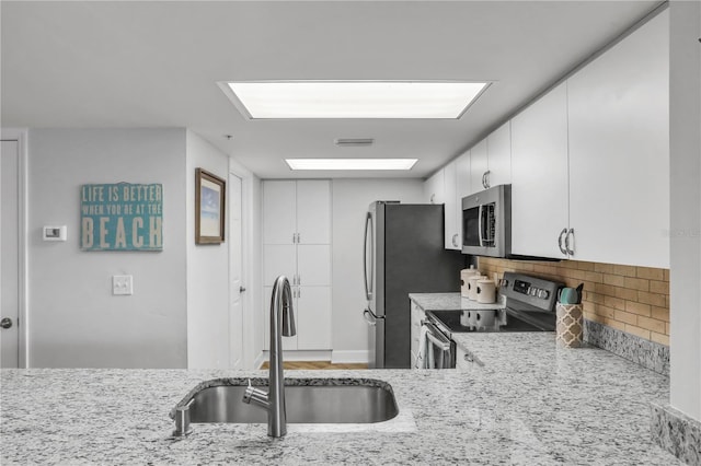 kitchen with light stone countertops, appliances with stainless steel finishes, tasteful backsplash, sink, and white cabinetry