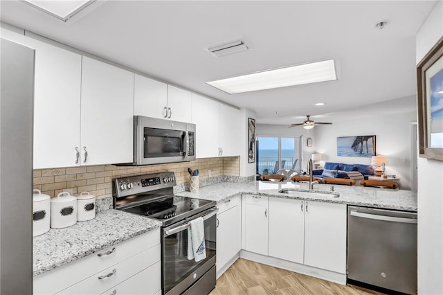 kitchen with sink, stainless steel appliances, light stone counters, white cabinets, and light wood-type flooring