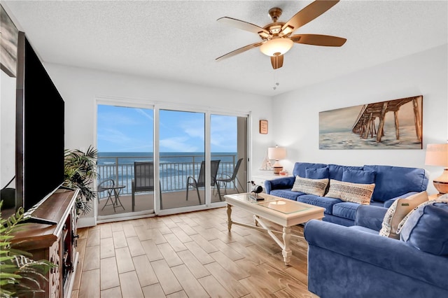 living room with a textured ceiling, a water view, ceiling fan, and light hardwood / wood-style floors