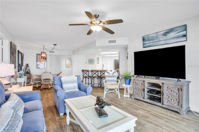 living room with ceiling fan with notable chandelier and light hardwood / wood-style flooring