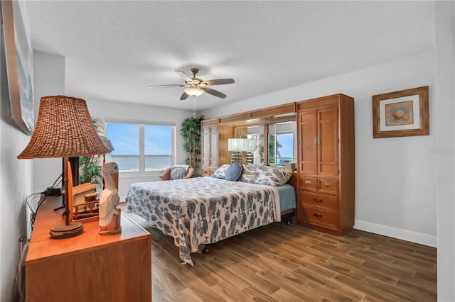 bedroom featuring a textured ceiling, ceiling fan, a water view, and dark hardwood / wood-style floors