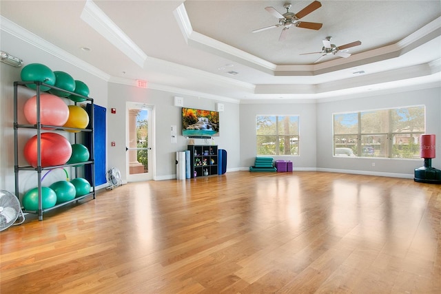 workout room with ceiling fan, a raised ceiling, light wood-type flooring, and ornamental molding