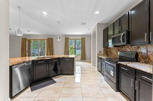 kitchen featuring sink, stainless steel appliances, light stone counters, backsplash, and pendant lighting