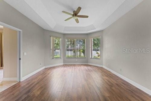 empty room with a tray ceiling, ceiling fan, and wood-type flooring