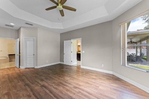 unfurnished bedroom with hardwood / wood-style flooring, multiple windows, a tray ceiling, and ceiling fan