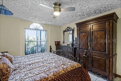 tiled bedroom with ceiling fan and a textured ceiling