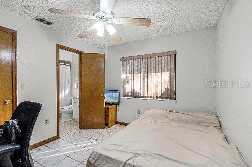 bedroom featuring ceiling fan, a textured ceiling, and ensuite bath