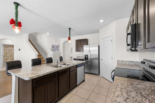 kitchen with a center island with sink, sink, a textured ceiling, appliances with stainless steel finishes, and dark brown cabinetry