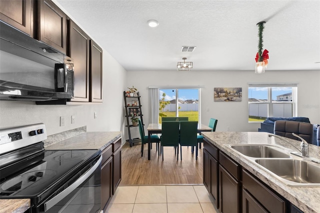 kitchen with sink, electric range, light tile patterned floors, a textured ceiling, and dark brown cabinetry