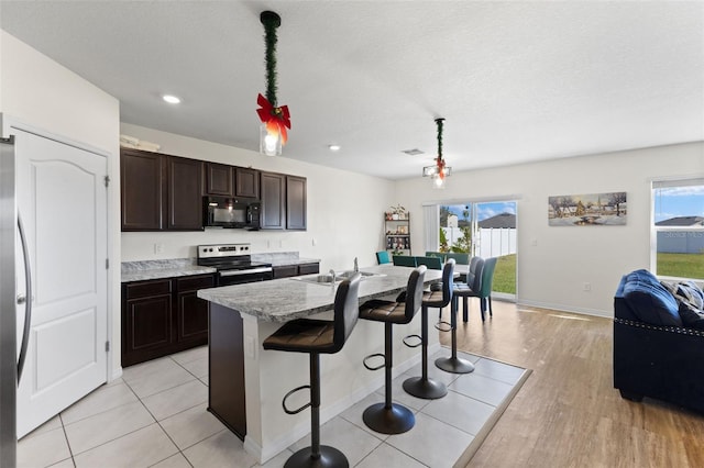 kitchen with stainless steel appliances, a kitchen breakfast bar, light hardwood / wood-style flooring, an island with sink, and dark brown cabinets