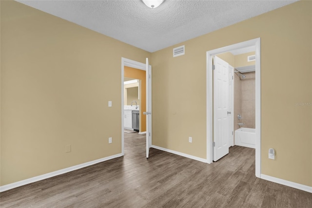 unfurnished bedroom featuring ensuite bathroom, a textured ceiling, sink, a spacious closet, and hardwood / wood-style floors