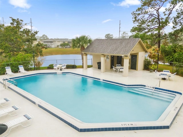 view of swimming pool featuring an outbuilding, a water view, and a patio