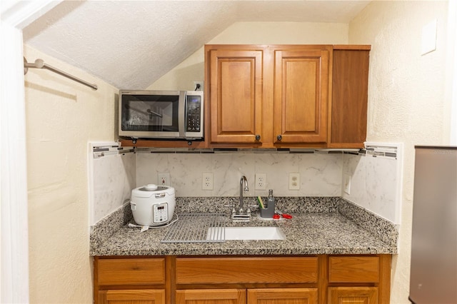 kitchen with stone counters, sink, vaulted ceiling, decorative backsplash, and a textured ceiling