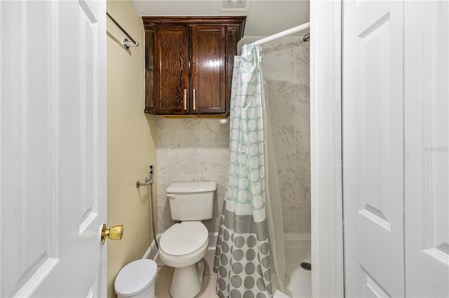 bathroom with toilet, curtained shower, and tile walls