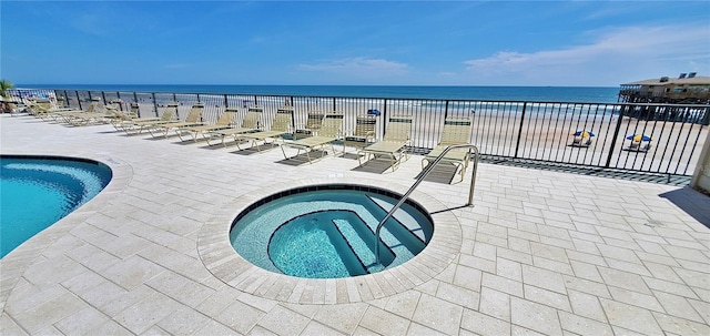 view of pool featuring a patio area, a water view, a beach view, and a hot tub