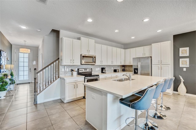 kitchen with a breakfast bar, a kitchen island with sink, white cabinets, sink, and appliances with stainless steel finishes