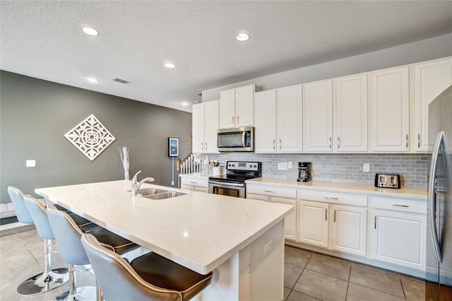 kitchen featuring white cabinetry, sink, stainless steel appliances, an island with sink, and a kitchen bar