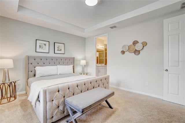 bedroom with light carpet, a textured ceiling, a tray ceiling, and ensuite bath