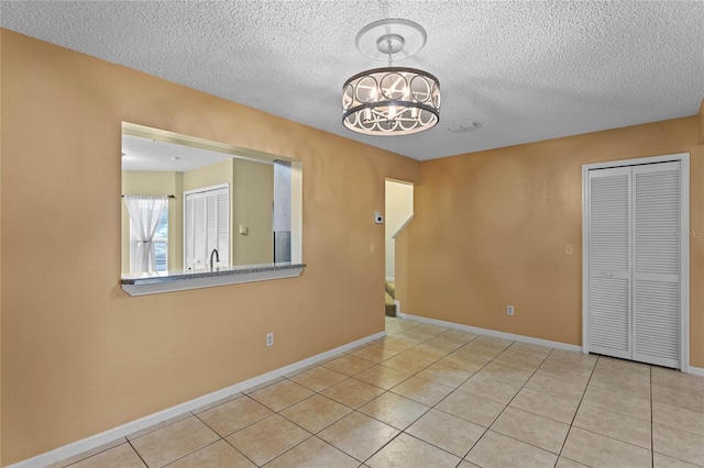 tiled empty room featuring a textured ceiling and a notable chandelier