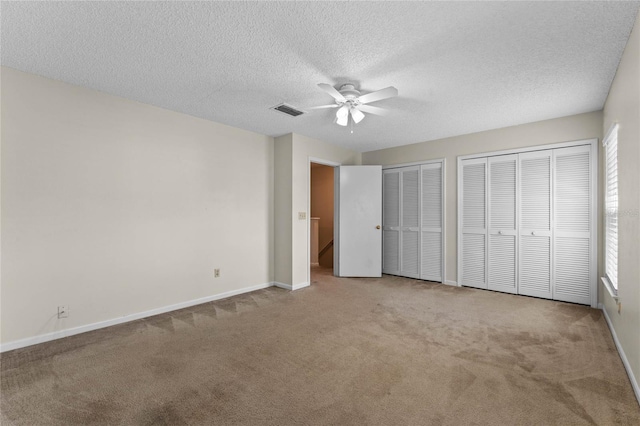 unfurnished bedroom featuring ceiling fan, light colored carpet, a textured ceiling, and two closets