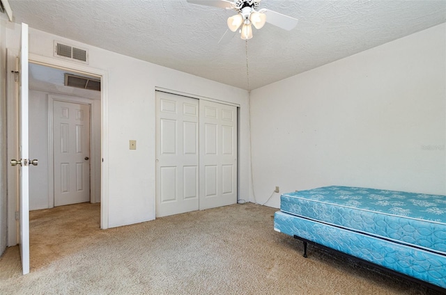 carpeted bedroom with ceiling fan, a textured ceiling, and a closet