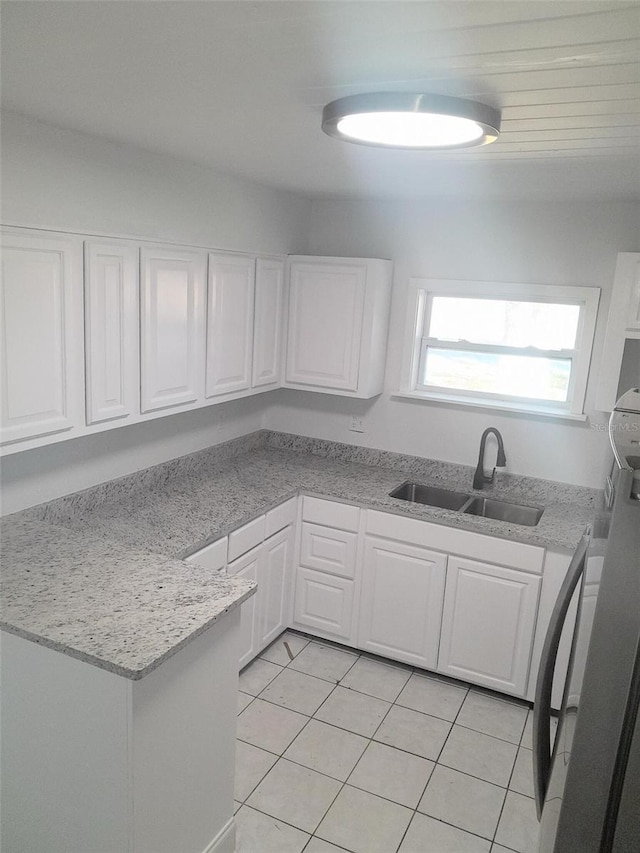 kitchen featuring light tile patterned flooring, light stone counters, white cabinetry, and sink