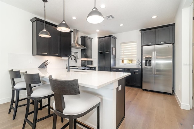 kitchen with kitchen peninsula, appliances with stainless steel finishes, hanging light fixtures, wall chimney exhaust hood, and sink