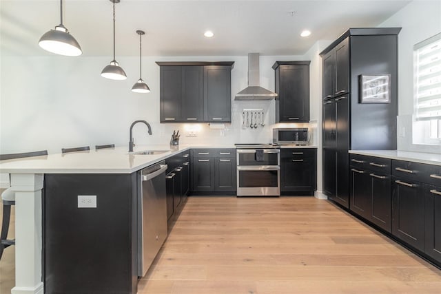 kitchen with decorative light fixtures, wall chimney range hood, stainless steel appliances, sink, and a breakfast bar area