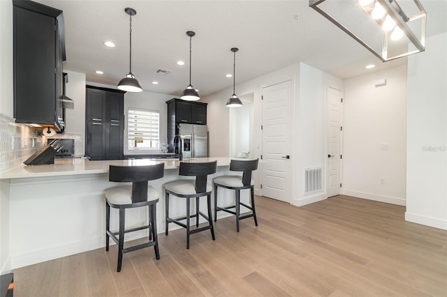 kitchen with pendant lighting, kitchen peninsula, tasteful backsplash, and stainless steel fridge