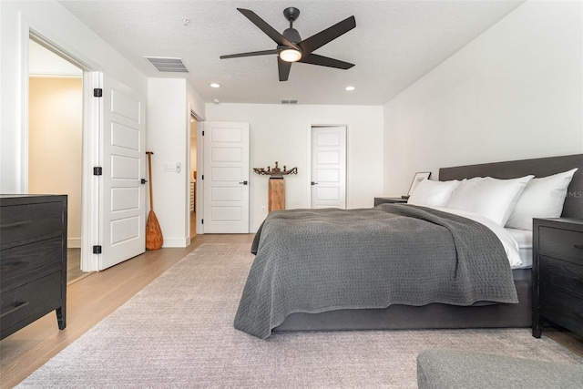 bedroom with light wood-type flooring, ceiling fan, and a textured ceiling