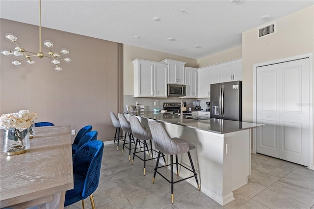 kitchen featuring kitchen peninsula, appliances with stainless steel finishes, a kitchen breakfast bar, decorative light fixtures, and white cabinets