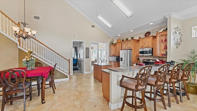 kitchen with high vaulted ceiling, a notable chandelier, a breakfast bar area, appliances with stainless steel finishes, and ornamental molding