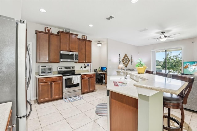 kitchen featuring appliances with stainless steel finishes, a kitchen breakfast bar, ceiling fan, a kitchen island with sink, and sink